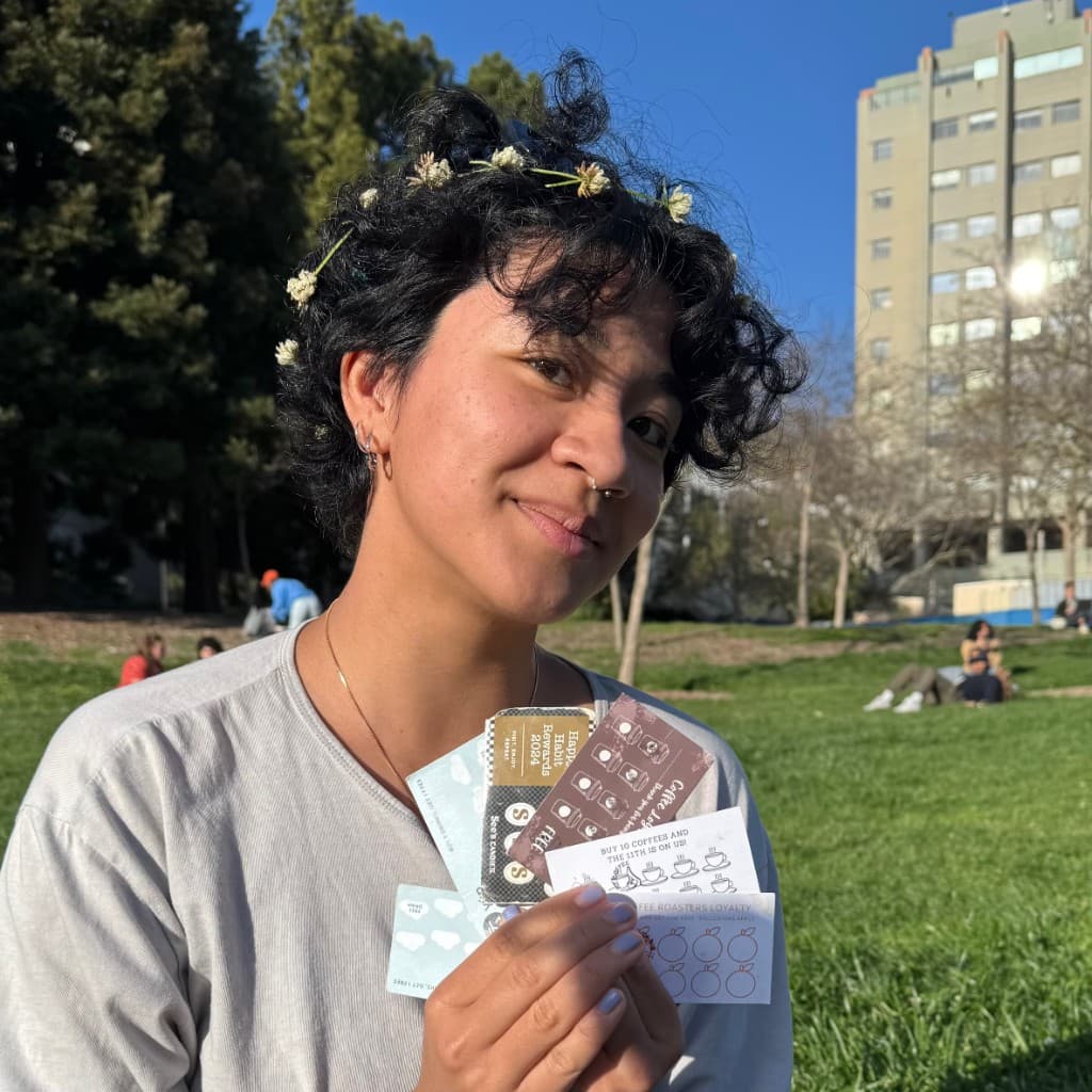 Person holding a fan of paper loyalty punch cards from multiple cafés